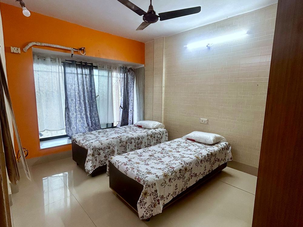 A sharing room with beds set apart, a curtained window and a warm accent wall